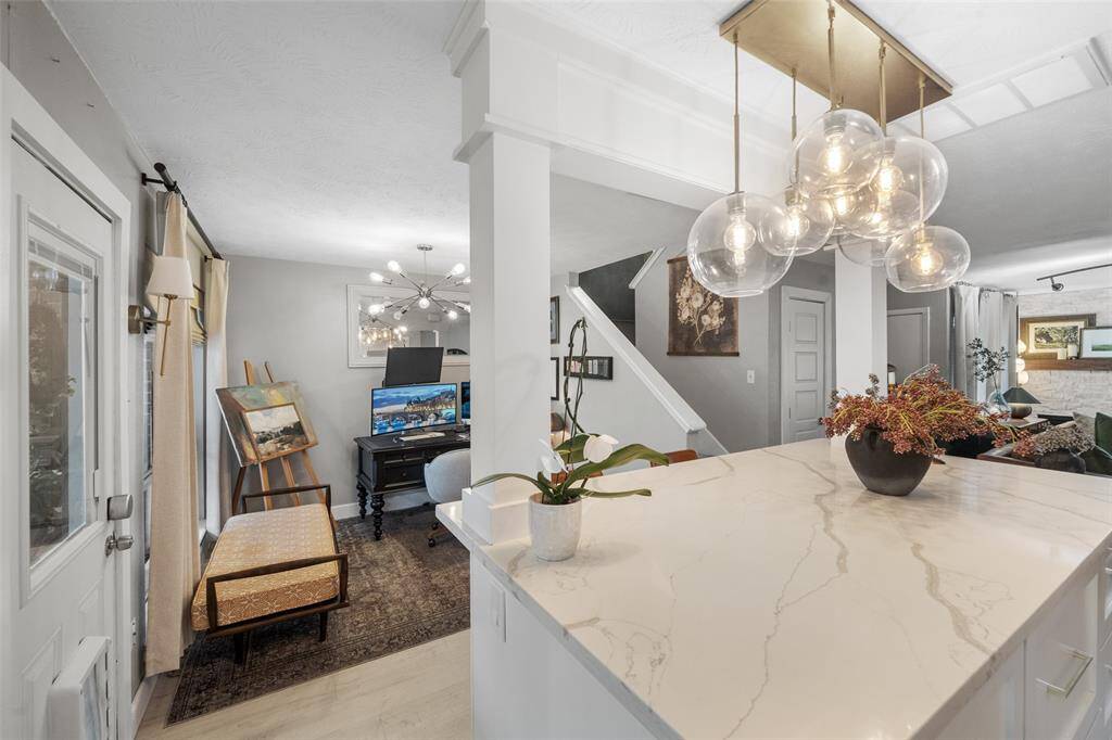 This photo showcases a modern, open-concept living area featuring a sleek kitchen island with elegant lighting fixtures. The space includes a cozy workspace, contemporary decor, and ample natural light, creating a welcoming and stylish environment.