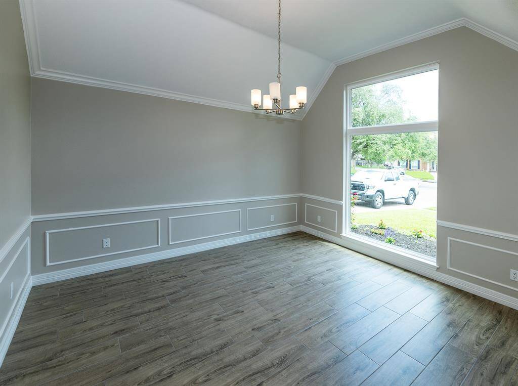 This room features a bright, open space with large windows and wood-style flooring. Elegant wainscoting and a modern chandelier add a touch of sophistication, ideal for a dining or living area.