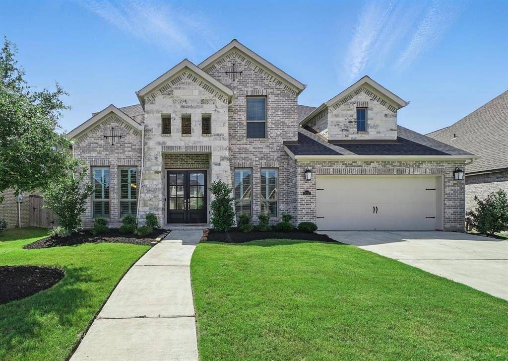 Stately two-story brick and stone exterior with three gables and a welcoming front entry. Manicured landscaping and a wide driveway lead to the attached 3-car garage.