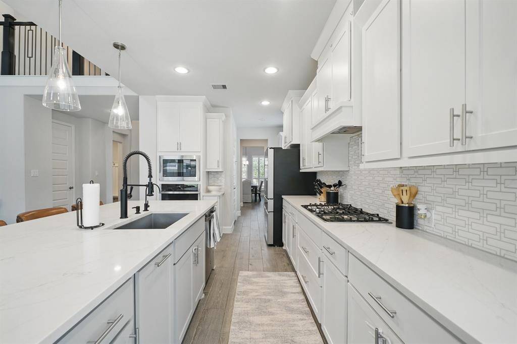 A galley-style view of the kitchen highlights the double oven, sleek gas cooktop, and extended counter space flowing into the main living areas.