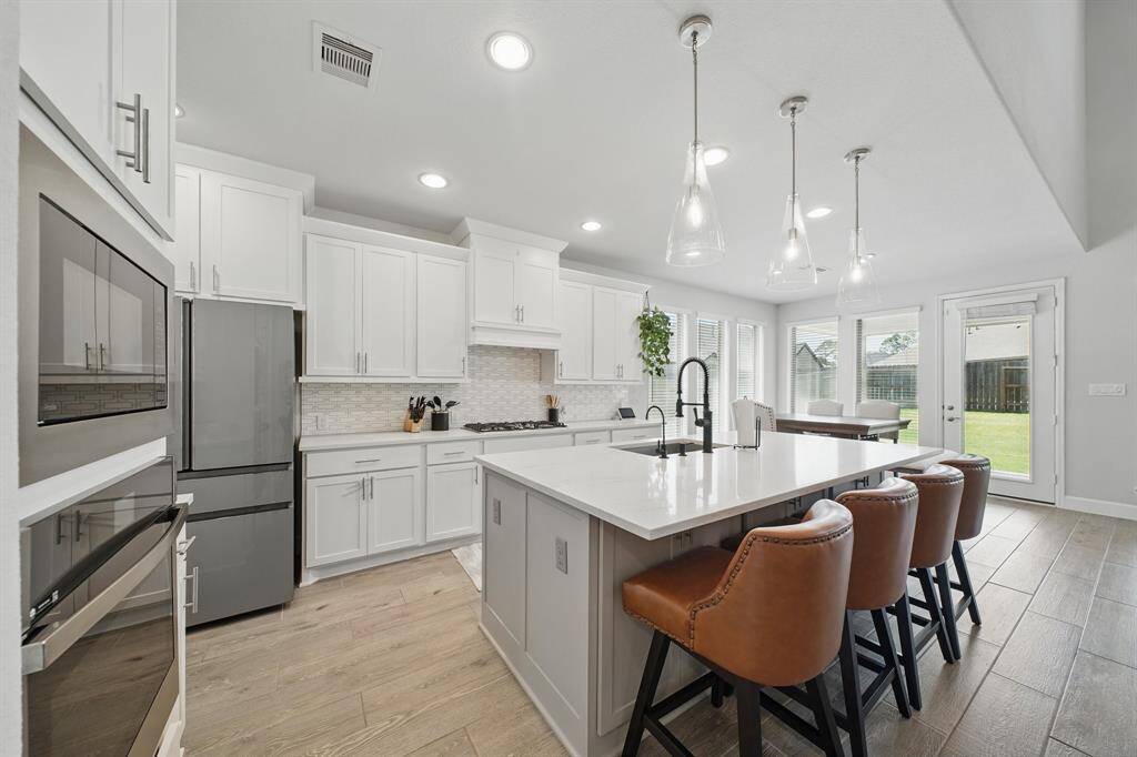This angle highlights the full kitchen layout, bar seating, and access to the breakfast area and backyard, all drenched in natural light.