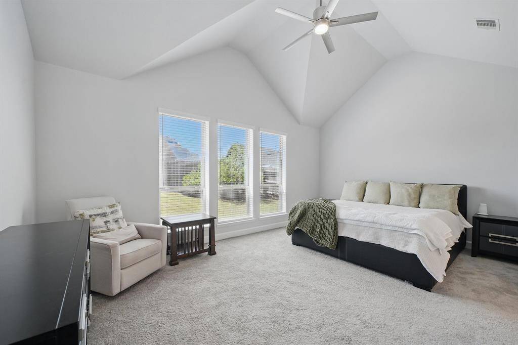 The spacious primary bedroom features vaulted ceilings, neutral tones, and a trio of large windows that fill the room with natural light and backyard views.