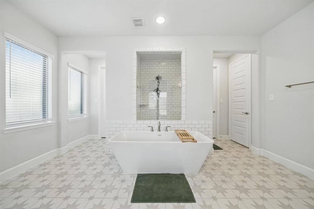 This luxurious bathroom includes a soaking tub set beneath a custom-tiled alcove shower, with natural light streaming in through dual windows.