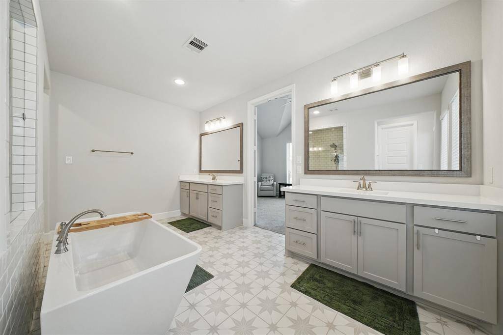 Dual vanities with framed mirrors and ample storage sit across patterned tile flooring, offering both function and elegance in the primary ensuite.