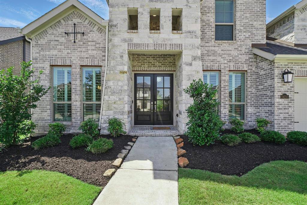A covered front porch with double glass-panel doors anchors the entry, surrounded by neatly landscaped beds and full-view windows with plantation shutters.