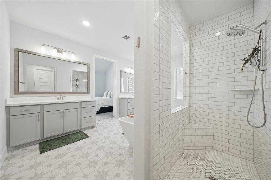 A detailed view of the primary walk-in shower reveals custom subway tile, a rainfall shower head, built-in bench, and window for natural light.