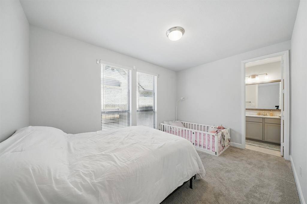 This downstairs bedroom features soft carpet, natural light from dual windows, and direct access to a full bath—ideal for guests or multi-generational living.