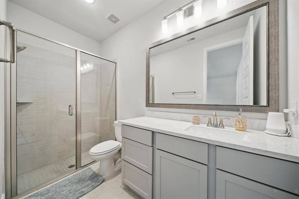 The adjacent full bath includes a walk-in shower with sliding glass doors, framed mirror, and a spacious vanity with under-sink storage.