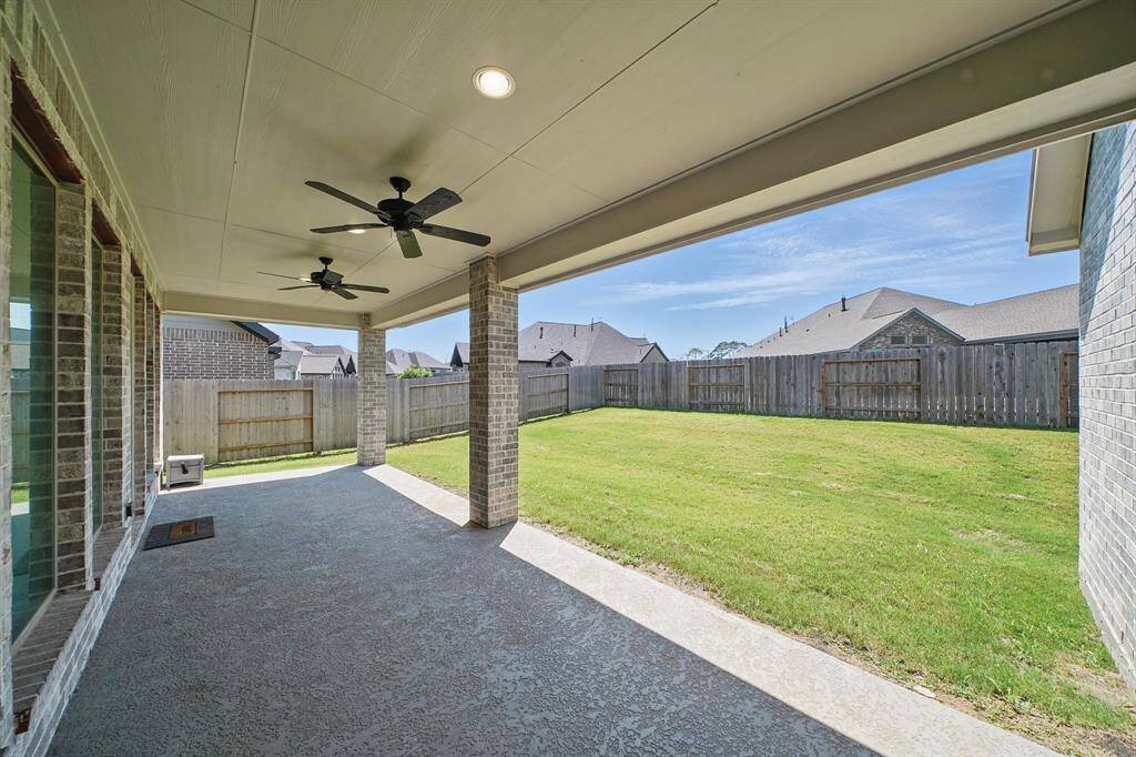 Covered back patio with dual ceiling fans and extended concrete slab—offering a shaded space for outdoor living with views of the fully fenced yard.
