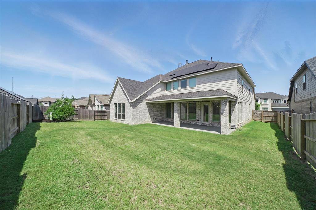 Another angle of the generous backyard, showcasing the full width of the lot and the home's covered patio with dual ceiling fans.