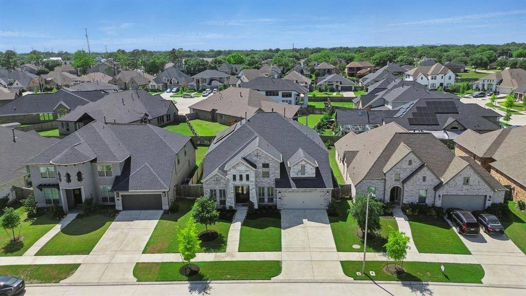 Front aerial view showcasing the home’s curb appeal, extended driveway, and its placement within a well-maintained, upscale neighborhood.