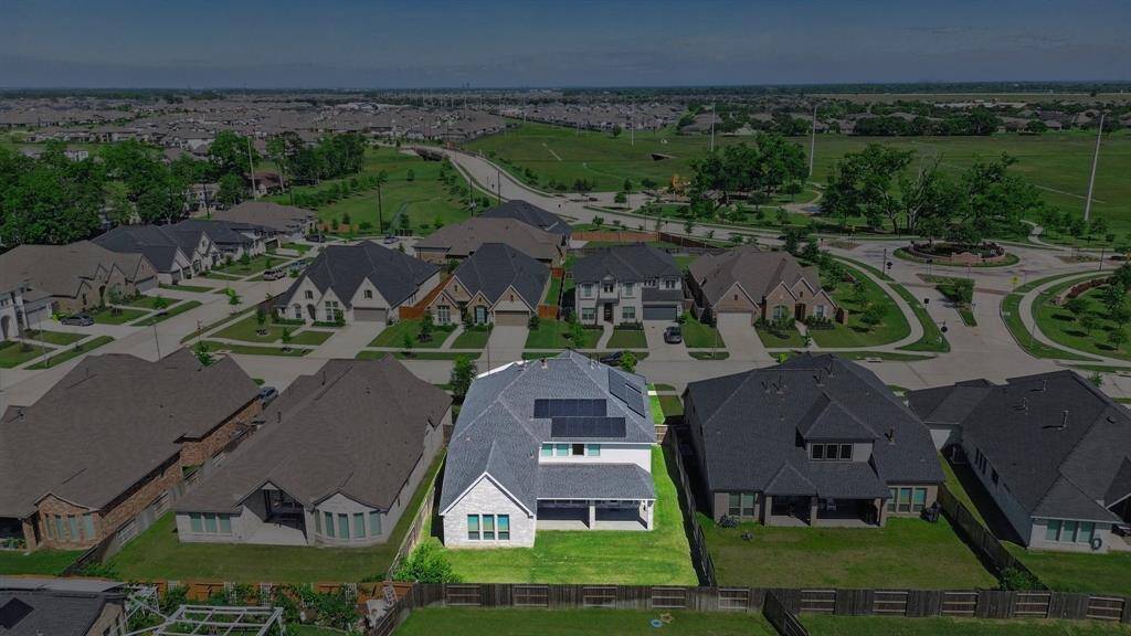 Rear aerial shot with the property highlighted—displaying the expansive backyard, covered patio, and roof-mounted solar panels.