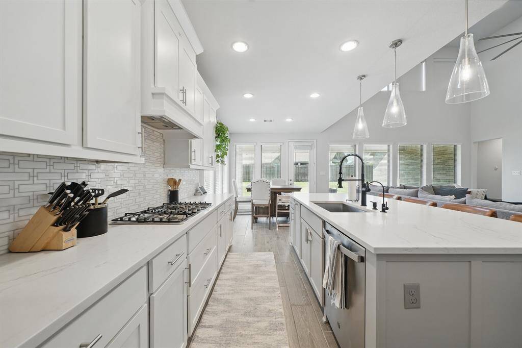 This open-concept kitchen showcases a large island with pendant lighting, gas cooktop, quartz countertops, and a seamless flow into the dining area and family room, all with views to the backyard.