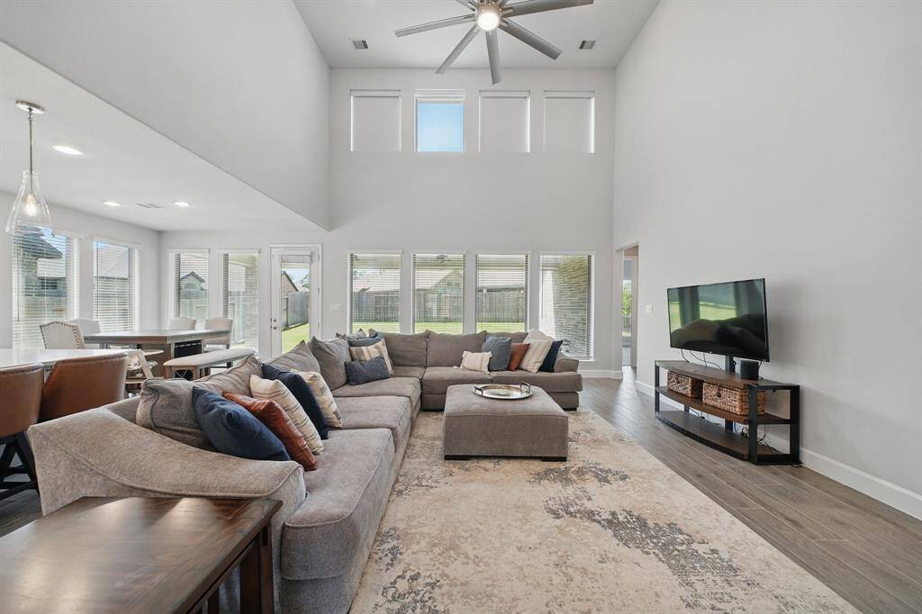 A two-story family room offers expansive vertical space, modern ceiling fan, and backyard views through multiple full-height windows that flood the room with light.