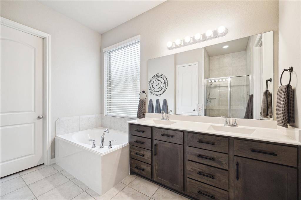 This bathroom features a modern design with a spacious double vanity, large mirror, and elegant lighting. It includes a relaxing soaking tub, the perfect ending to a long day.