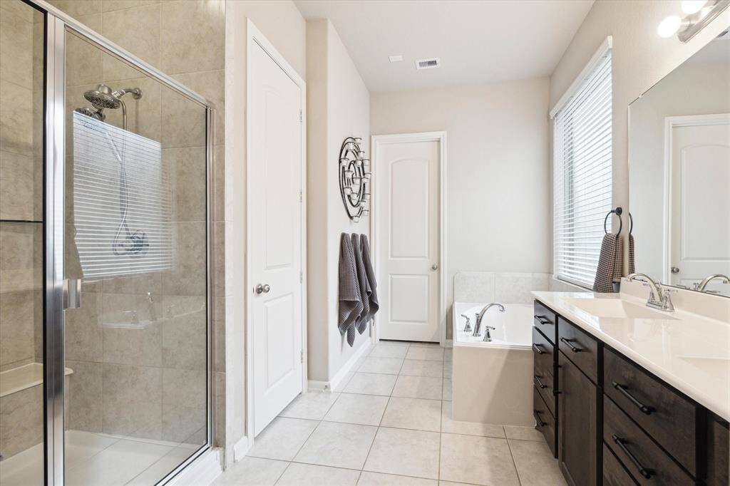 This bathroom features a spacious walk-in shower, a separate bathtub, dual sinks with dark wood cabinetry, and ample natural light from a large window.