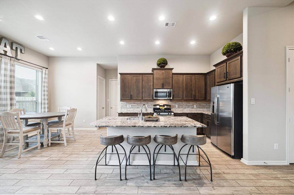 This bright kitchen features modern stainless steel appliances, granite countertops, and a spacious island with seating. It opens to a cozy dining area with large windows, offering plenty of natural light.