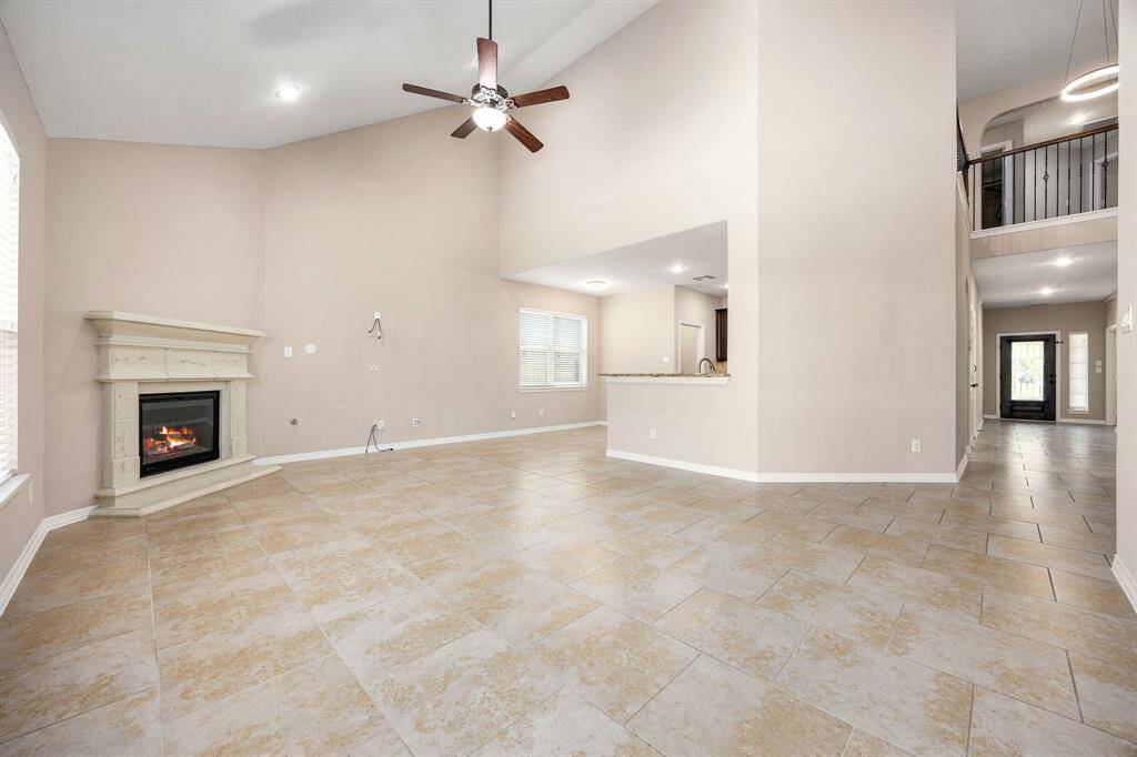 Spacious living room with soaring ceilings, tile flooring, and a cozy corner fireplace. An open-concept layout connects seamlessly to the kitchen.