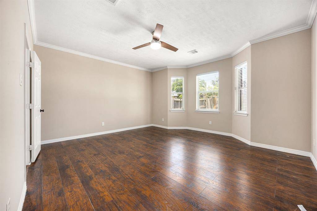 Large primary bedroom features wood-look vinyl plank flooring, crown molding and a ceiling fan.