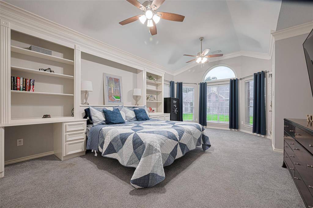 The spacious primary suite offers bay windows that flood the room with natural light, a cozy sitting area, and built-in bookcases with a custom headboard spanning one wall—creating a perfect blend of comfort and functionality