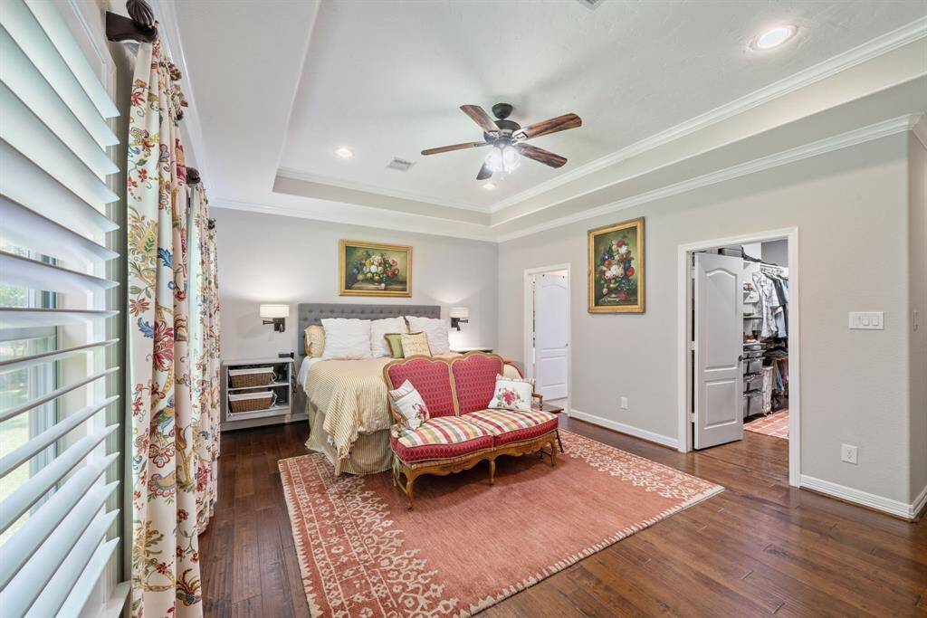 Rich wood floors and a tray ceiling enhance this spacious primary bedroom, which includes a full-entry closet for added function.