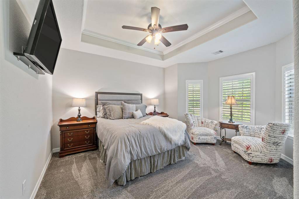 Another generously sized bedroom features soft carpet underfoot, large windows, and a tray ceiling with ceiling fan.