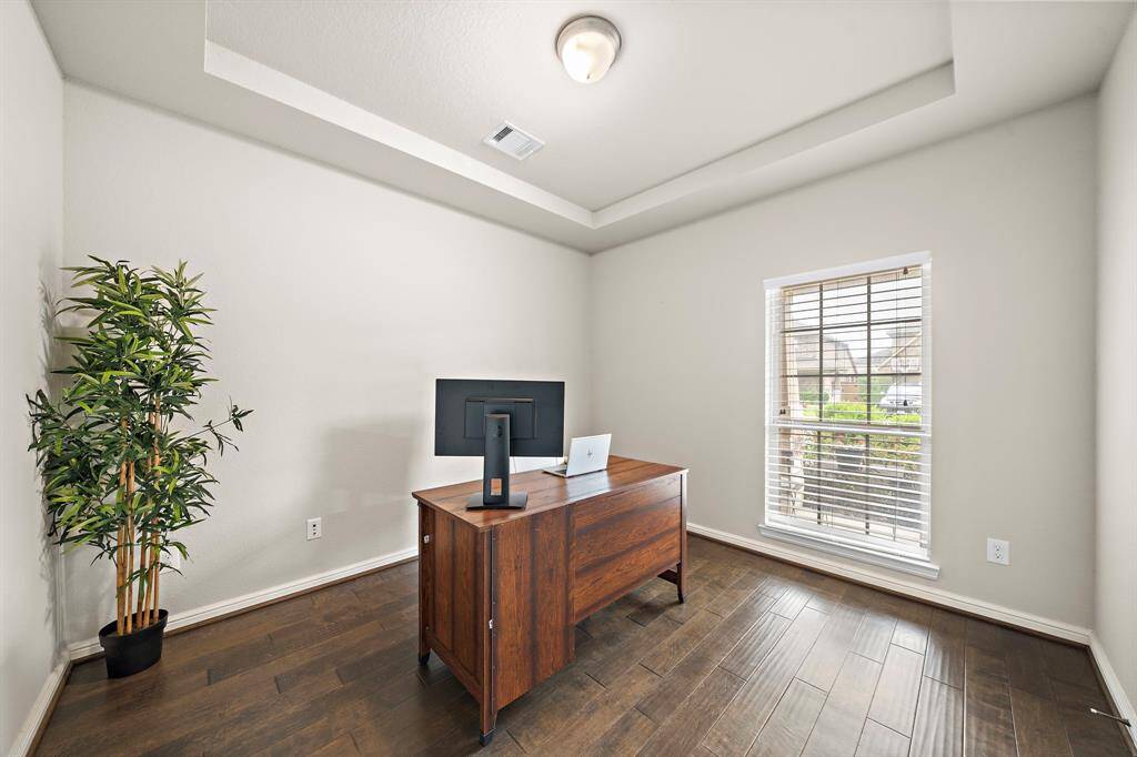 The home office is located at the entryway of the home and features tray ceilings and engineered hardwood floors.