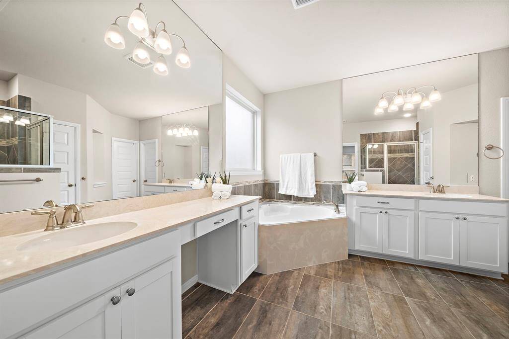 The primary bathroom features double sinks, quartz countertops, a vanity sitting area, a serpate walk-in shower, and soaking tub.
