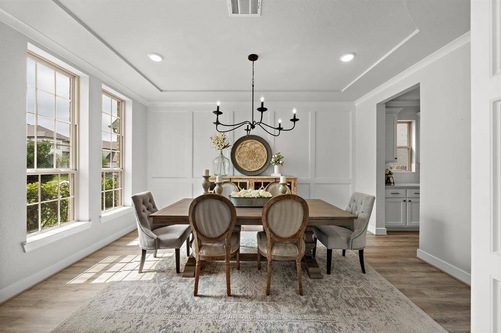 Formal dining room located at the entryway of the home features a custom accent wall, upgraded chandelier, crown molding, and tray ceilings.