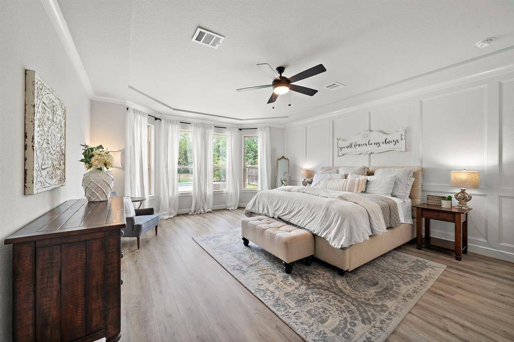 Primary bedroom retreat featuring bay windows, a sitting area, custom accent wall, crown molding, and luxury vinyl plank floors.