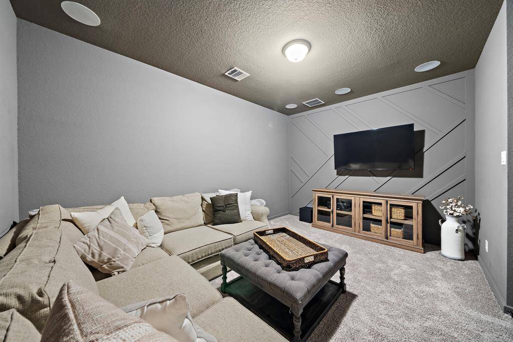 Media room located on the second floor features a dark ceiling, built-in speakers, and a custom accent wall.