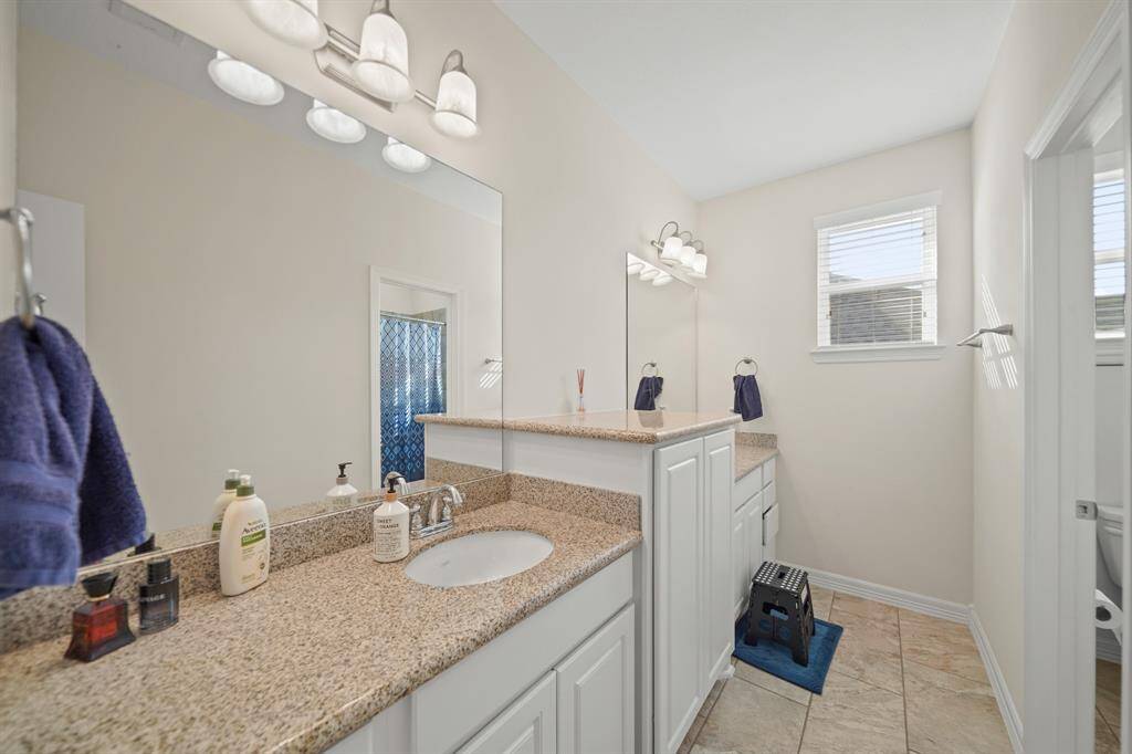 Secondary bathroom with double sinks, granite countertops, a large mirror, and tile floors.
