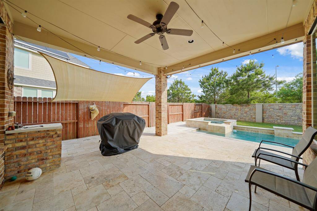 Enjoy a great barbecue on your amazing covered patio, featuring a high ceiling with a ceiling fan, and brick accent wall.
