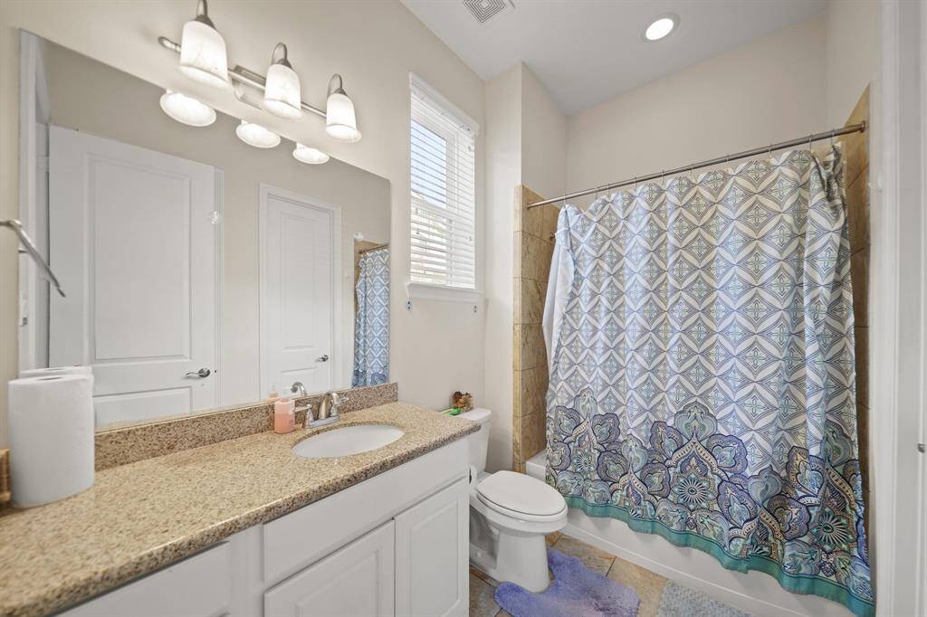 Secondary bathroom with granite countertops and backsplash, a large mirror, and shower/tub combo.