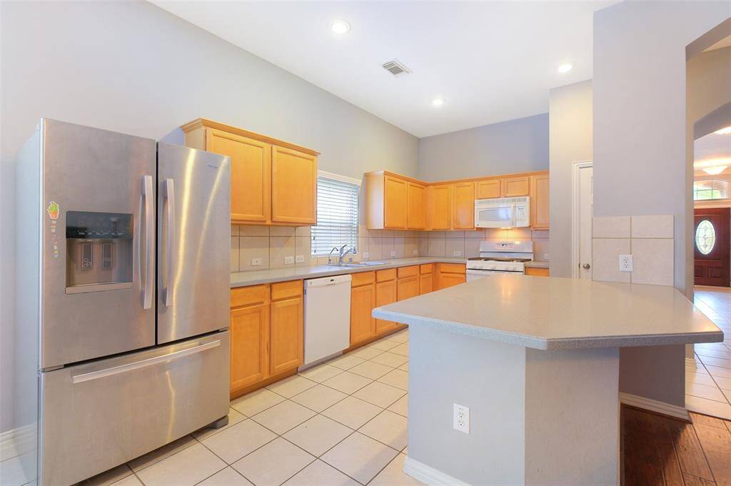 Spacious kitchen featuring warm maple cabinetry, a gas range, and a peninsula with bar seating space—perfect for casual meals or entertaining. The open-concept layout flows effortlessly from the front entrance, through the living and dining areas, and into the heart of the home.