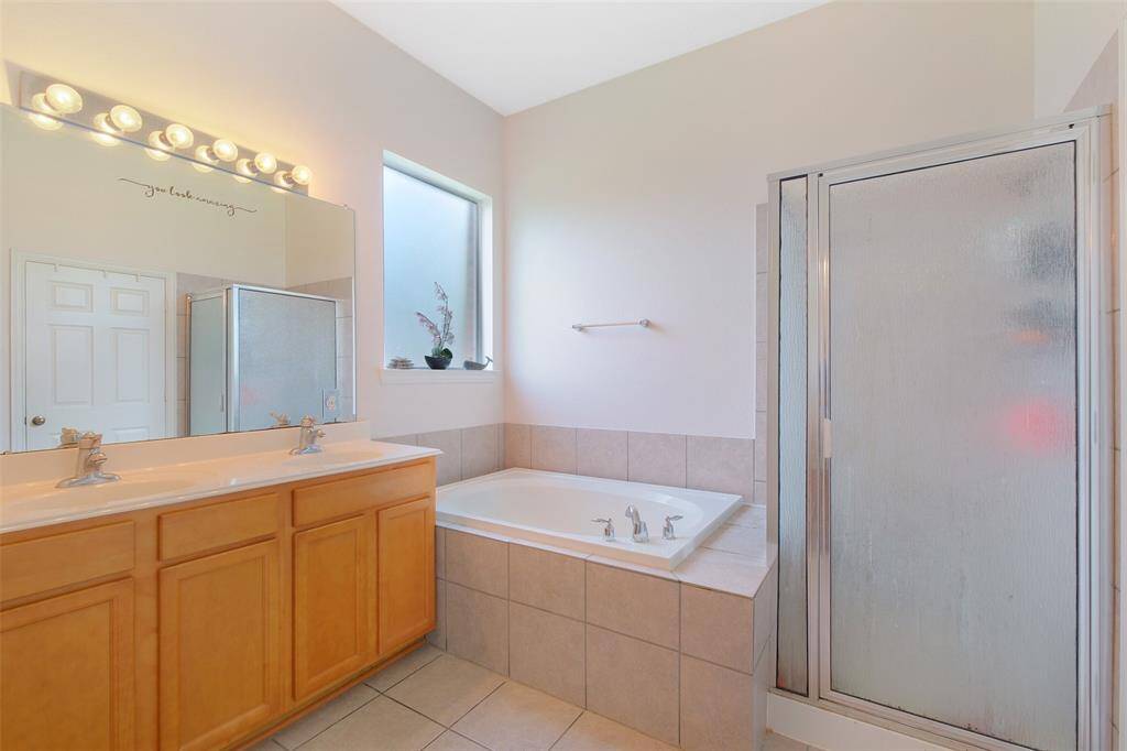The en-suite master bathroom features a relaxing soaking tub beneath a privacy window, separate walk-in shower, dual sinks with an extended vanity, and plenty of natural light to brighten your morning routine.