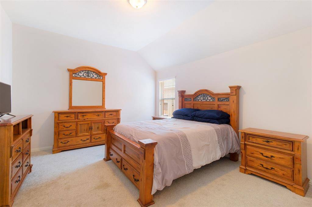 This first-floor secondary bedroom offers comfort and flexibility, featuring neutral tones, plush carpeting, an elevated gambrel ceiling, and a large window that fills the space with natural light.