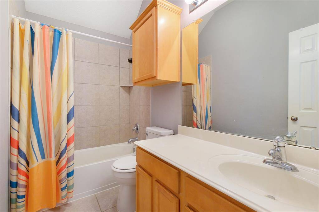 This full bathroom on the first floor features a tile-surround shower and tub combo, extended vanity with ample counter space, and additional storage cabinetry—conveniently located to serve guests and secondary bedrooms.