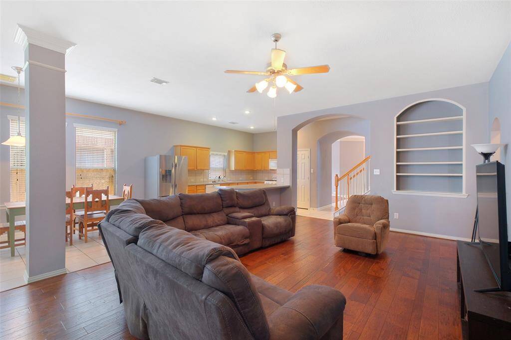 Continue into a spacious family room with warm wood flooring, built-in shelving, and open sightlines to the kitchen and breakfast area—perfect for everyday living and entertaining. Arched doorways and crown molding add architectural charm.