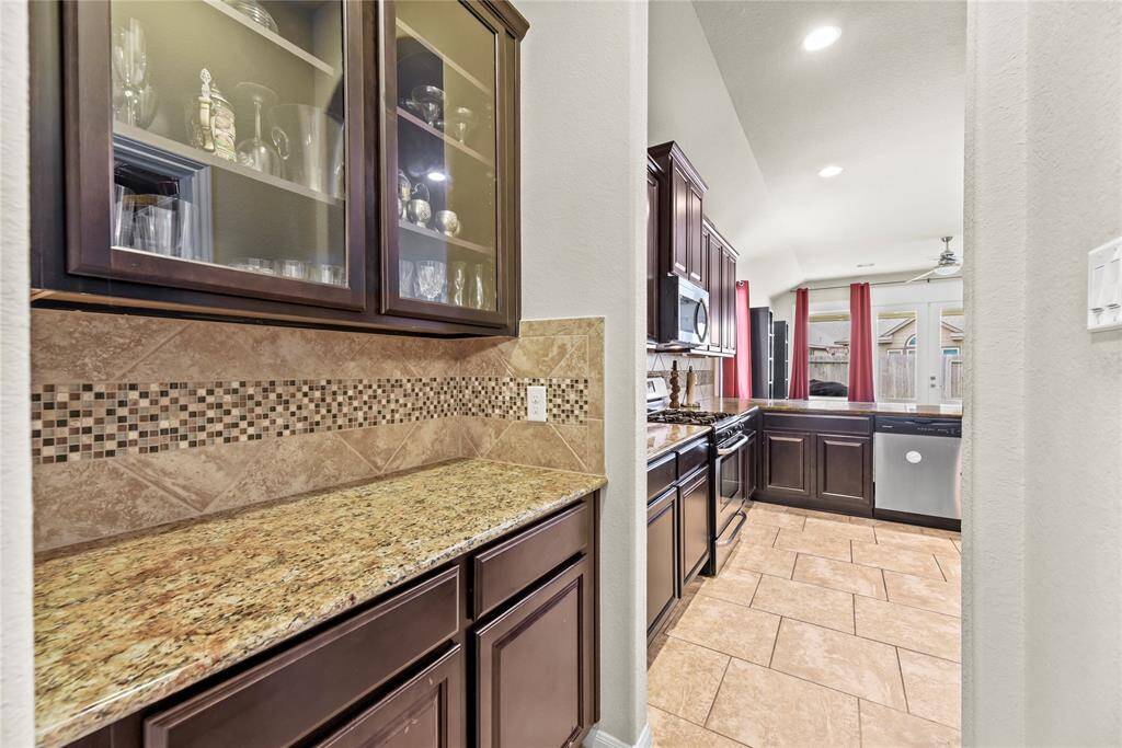 The butler’s pantry features glass-front cabinetry perfect for displaying stemware, complemented by sleek granite countertops and a stylish tile backsplash that adds both function and flair.