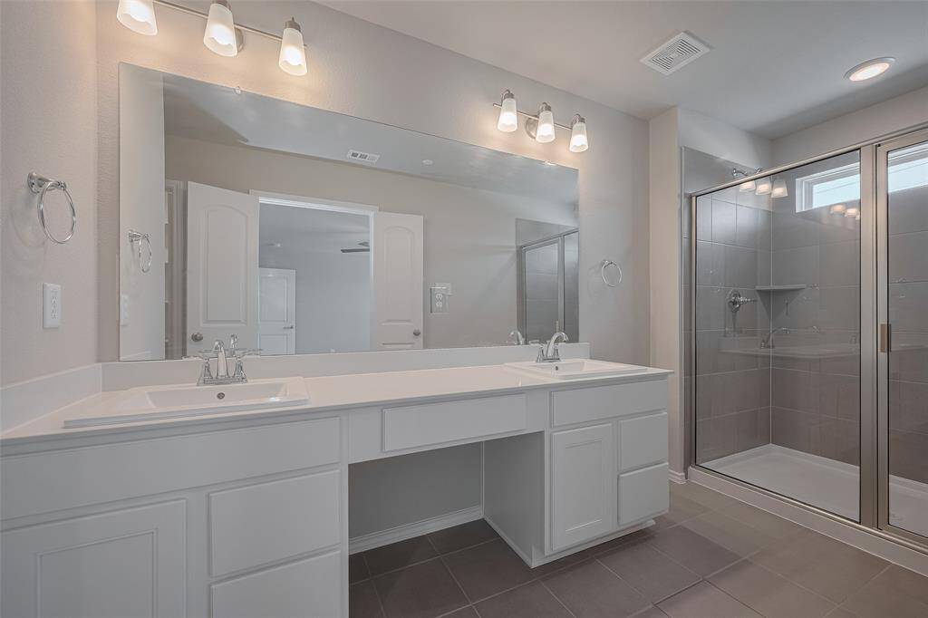 The primary bath showcases stylish gray tile, double vanities, and sleek chrome fixtures for a modern, polished look.