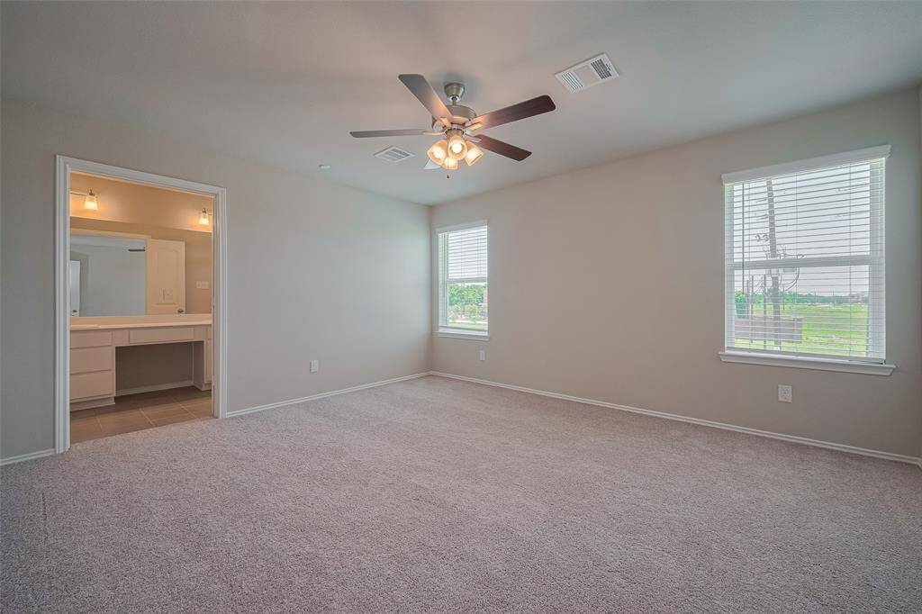 The primary bedroom is generously sized and filled with natural light from two large windows. It features brand-new carpet and a ceiling fan for added comfort.