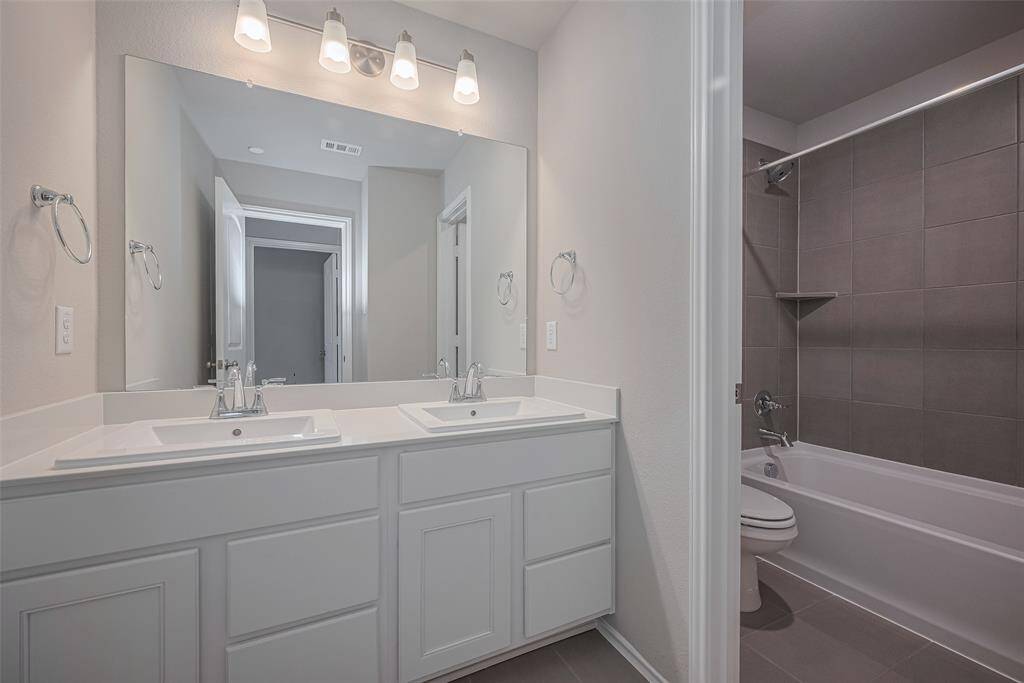 The shared bathroom is generously sized and features sleek chrome fixtures, modern gray tile, and double vanities. A separate door leads to a shower/tub combo, providing added privacy and functionality.