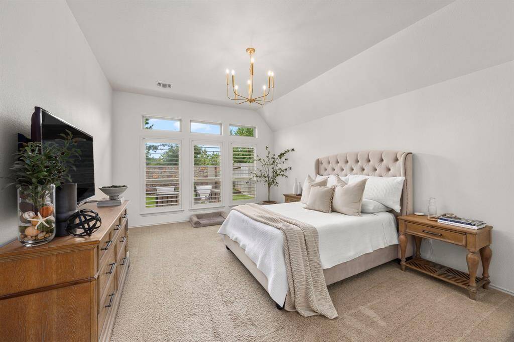 Impressive primary bedroom with oversized windows, custom plantation shutters and modern chandelier.