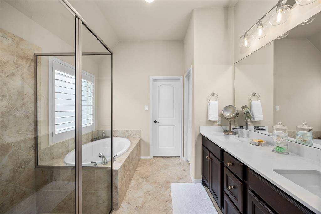 Spacious primary bath with separate tub and shower, dual sinks, custom plantation shutters, with clean sleek countertops and custom lighting.