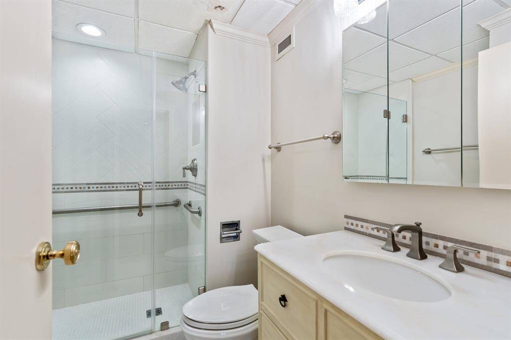 Renovated primary bathroom with an oversized seamless glass shower and marble top vanity.