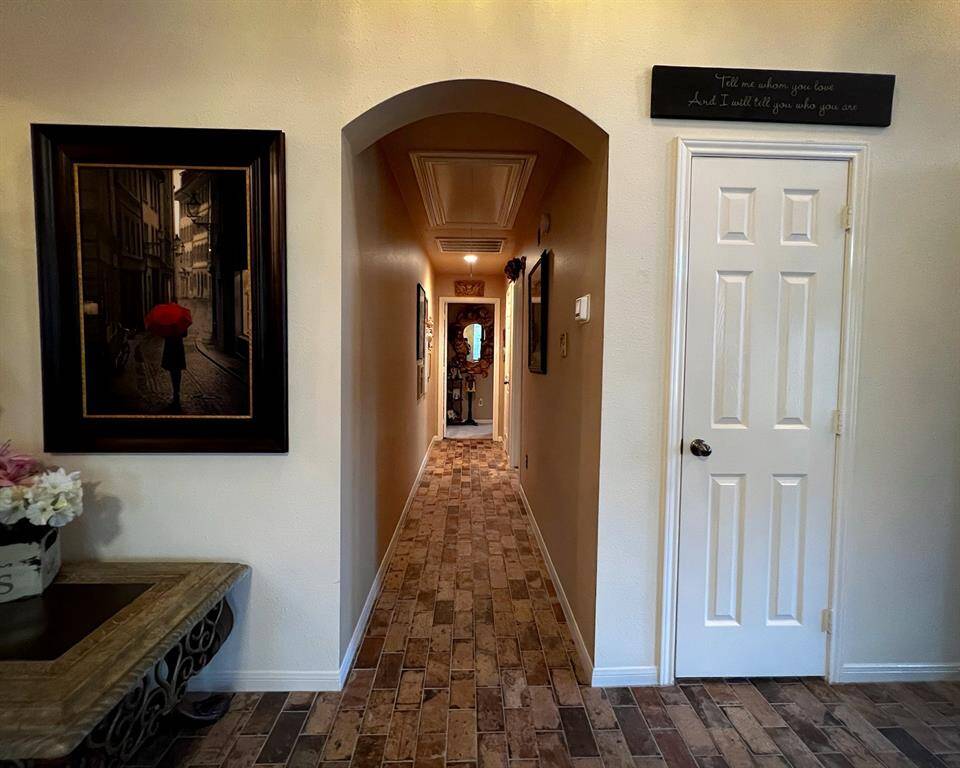 The hallway features a warm, inviting design that continues with the brick-style flooring. It leads to the secondary bedrooms rooms, with a cozy archway adding character to the space.