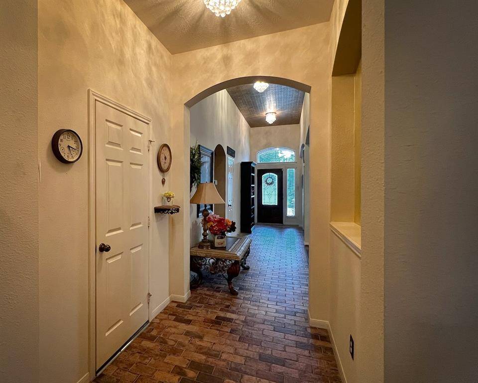 This view shows the interior access to the garage, charming brick floor, wide hallway, elegant archways, and glamorous light fixtures.