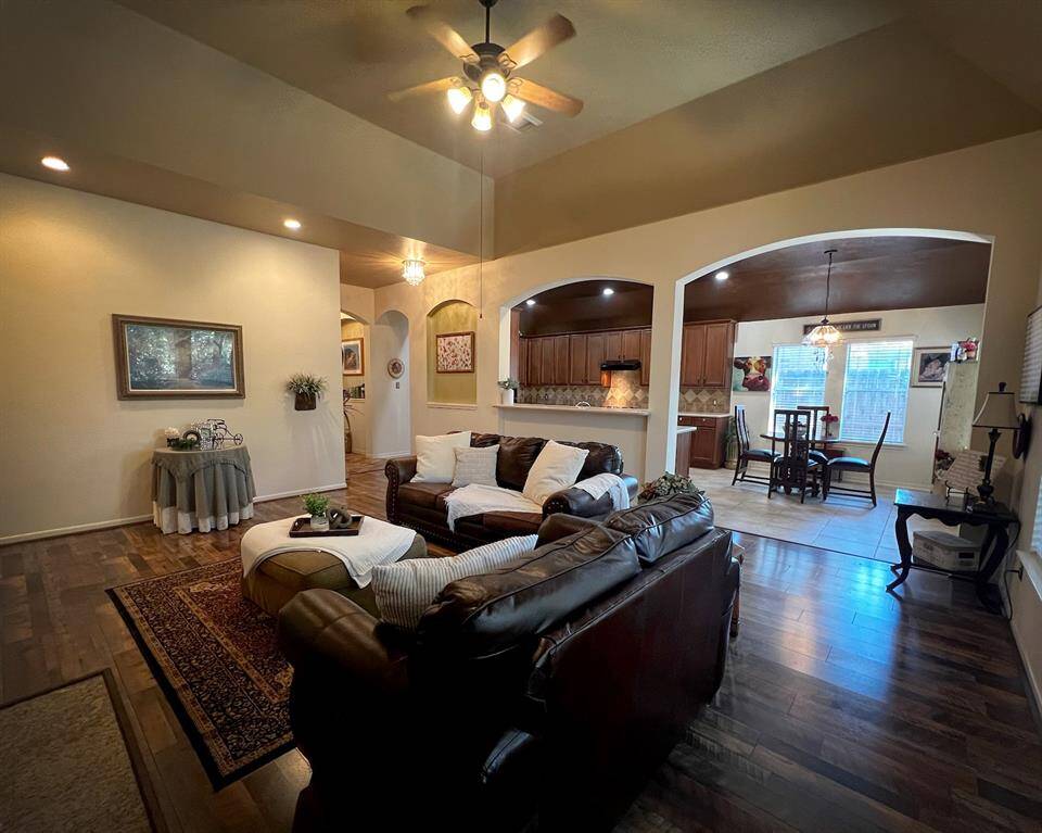 This spacious living room features newer elegant flooring (2021), ample space, and high, vaulted ceiling with recessed lighting. It seamlessly connects to a modern kitchen and dining space, creating an inviting and open atmosphere perfect for entertaining.