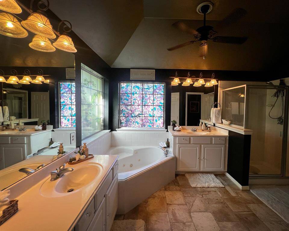 A roomy en-suite bathroom layout with dual sinks, dual vanities, large soaking tub, separate shower, high ceiling, and a beneficial bathroom ceiling fan. Relish in the recent tile flooring (2021), and a colorful stained-glass window that adds a touch of charm.